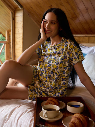 A woman in yellow Minion-print pajamas sits on a bed with a breakfast tray in front of her.