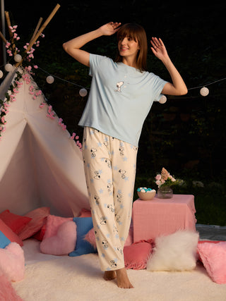 A woman in light blue Snoopy pajamas stands with her arms raised, posing playfully in an outdoor setting.