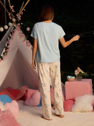 A woman wearing light blue Snoopy print pajamas stands facing away from the camera, with her arm extended towards a string of lights.