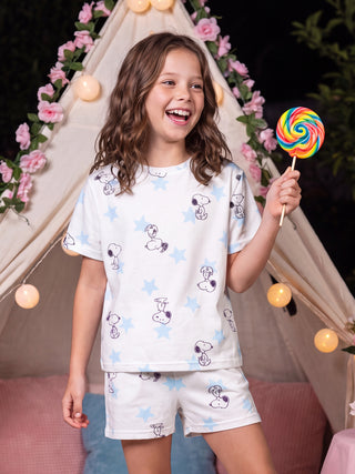 A young girl in a white Snoopy and star-print pajama set poses while holding a colorful lollipop.