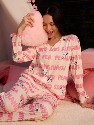 A young woman in a cream and pink Snoopy print pajama set is happily holding a pink heart pillow.