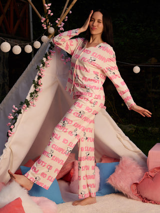 A woman in pink Snoopy-print pajamas poses playfully inside a teepee, winking with one eye and her hand on her forehead.