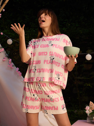 A woman in pink Peanuts Club printed sleepwear is posing with a bowl of food.