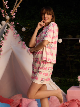 Women in a playful pose wearing a cream-colored short pajama set with a pink "Peanuts" print.