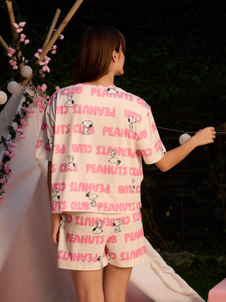 Women in a playful pose wearing a cream-colored short pajama set with a pink "Peanuts" print.