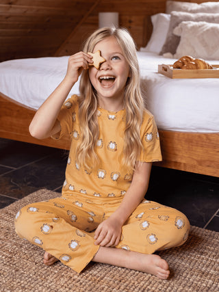 GIRLS in yellow Garfield print pajamas sitting on a rug, with one holding a star-shaped cookie over her eye.
