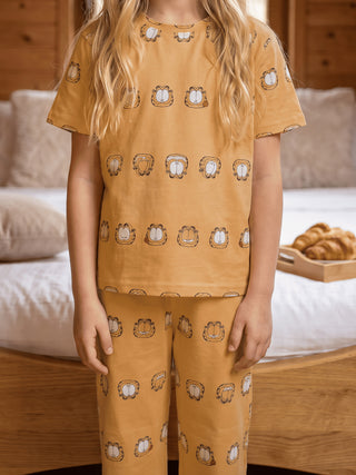 GIRLS' mustard yellow short-sleeve top and pants with an all-over Garfield print, worn by a child standing in front of a bed.