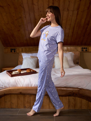 Women wearing a lilac polka dot pajama set featuring Garfield, standing next to a bed with a tray of breakfast.