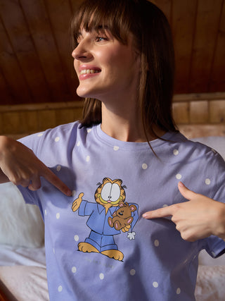 A woman poses wearing a light purple pajama top with white polka dots and a Garfield print, and she points to the graphic.
