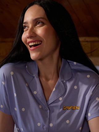A woman in lavender polka dot pajamas smiles looking up.