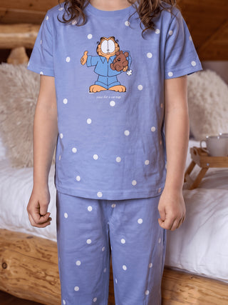 GIRLS, standing by a bed, wearing a light blue polka dot pajama set with Garfield printed on the top.