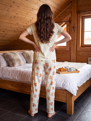 A woman stands with her back to the camera, wearing a cream-colored t-shirt and cream pajama pants with a pink Garfield print, with her hands on her hips.