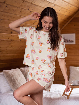 A woman wearing cream-colored Garfield print pajama shorts and a matching top poses playfully on a bed.