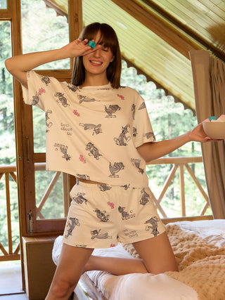 A woman kneels on a bed wearing white Tom and Jerry print sleepwear.