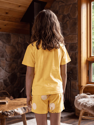 A young girl in yellow pajamas with a cartoon print stands facing away from the camera.