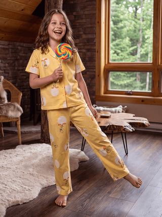 A young girl in yellow pajamas with a chick print poses with a lollipop.