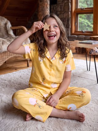Girls in yellow Tweety Bird print pajamas sit cross-legged on a rug, holding a star cookie to their eye.
