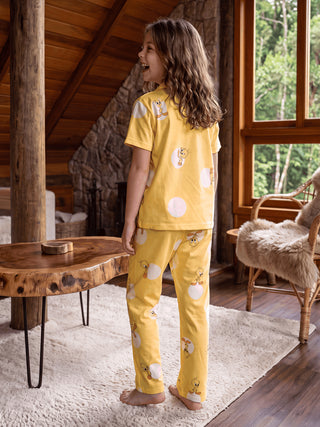 A young girl in yellow pajamas with Tweety Bird print stands with her back to the viewer, looking over her shoulder and smiling.
