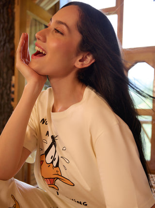 A woman with her hand on her chin wears a cream-colored short-sleeved t-shirt with a cartoon duck print.