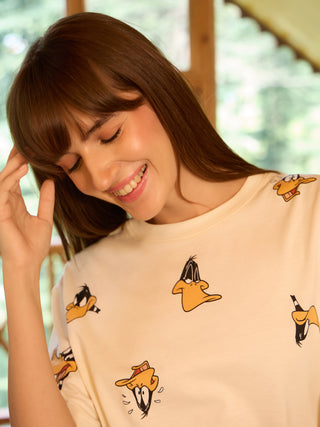 A woman in a cream-colored t-shirt with a cartoon duck print, smiling and looking down.