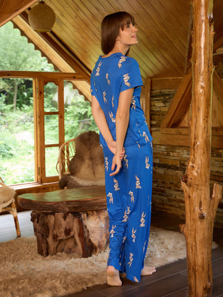 A woman models blue Bugs Bunny print pajamas, standing facing away from the camera and looking to the side, with her hands clasped behind her back.