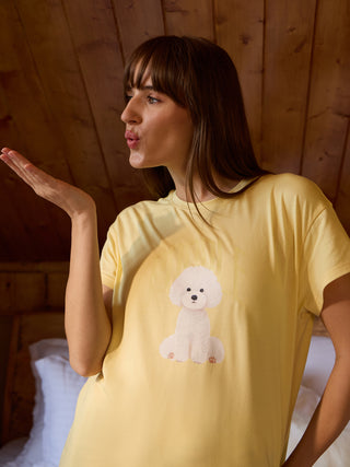 A woman blows a kiss while wearing a light yellow t-shirt with a white poodle print.