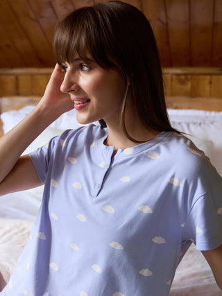 A woman poses in a light blue, short-sleeved pajama top with a cloud print.