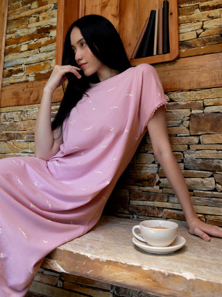 A woman lounges in a pink sleep dress with a bird print, a cup of coffee beside her.