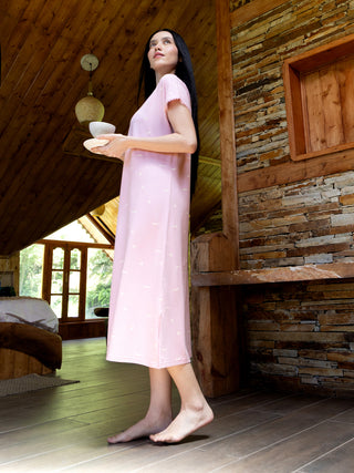 A woman in a pink nightgown with a floral print walks barefoot on a wooden floor.