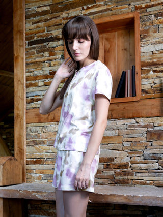 A young woman models a lavender and beige tie-dye pajama set, featuring a short-sleeved top and matching shorts.