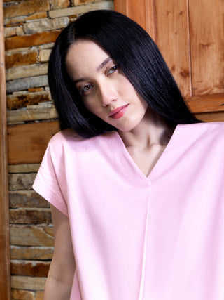 A woman with dark hair poses wearing a pink V-neck short-sleeve sleep shirt, unlike the previous image, her head is tilted to the side.