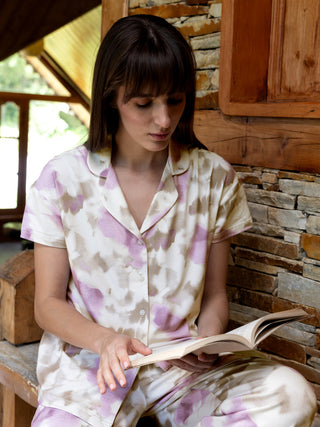 A woman wearing tie-dye pajamas reads a book.