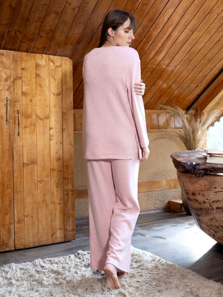 A woman in a pink sleepwear set stands with her back to the camera on a shaggy rug.