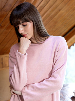 A woman wearing a pink long-sleeved sleepshirt rests her chin on her hand.