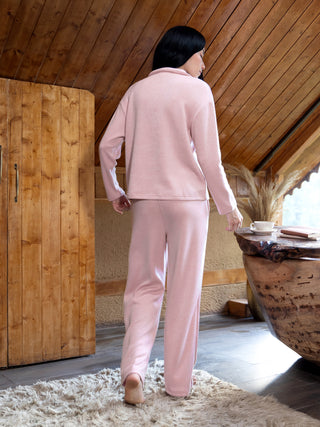 Women in a pink pajama set with a collared long-sleeve top and loose-fitting pants, standing and facing away from the camera on a fluffy rug.