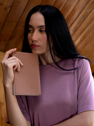 A woman in a purple crewneck sleep shirt holds a book to her chin.