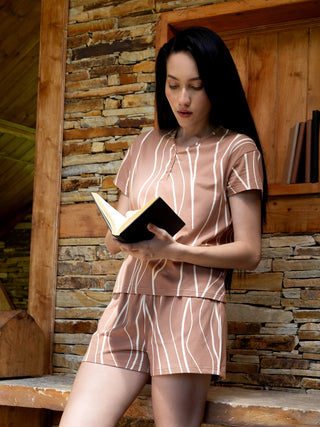 A woman in a brown striped pajama set reads a book against a stone wall.