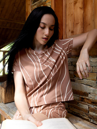 Woman in a brown striped pajama set, sitting and reading a book.