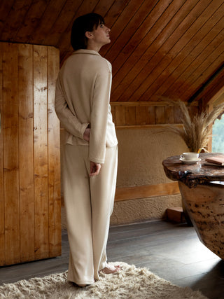 A woman stands with her back to the camera, wearing a cream-colored pajama set.