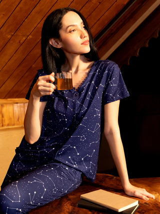 A woman in navy blue pajamas with a constellation print holds a mug of tea.