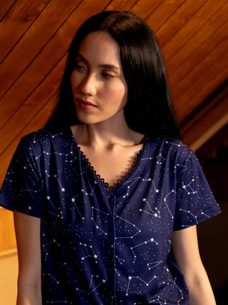 Women's navy blue sleep shirt with a white constellation print, posed looking away from the camera.