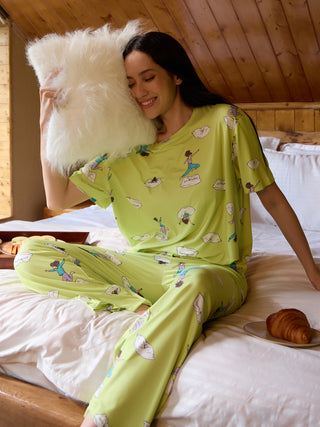 A woman in light green pajamas with a cartoon print rests with a fluffy pillow.