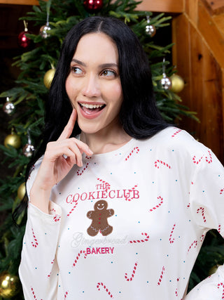 A woman wears a white pajama top with a gingerbread man and candy cane print.