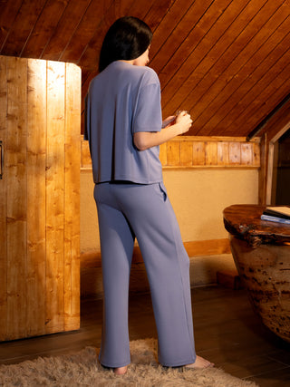 A woman in a periwinkle blue loungewear set holds a glass.