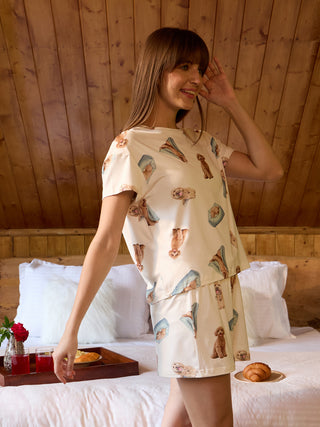 Woman in bed wearing cream colored pajamas with a playful dog print.