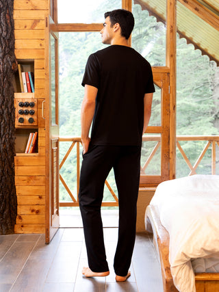 Men wearing black sleepwear, standing with back to camera, facing a window.