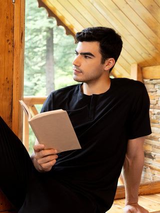 Men wearing black sleepwear, sitting and reading a book by a window.