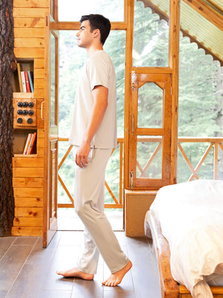 A young man stands facing away from the camera, wearing a light grey short-sleeved shirt and matching pants.