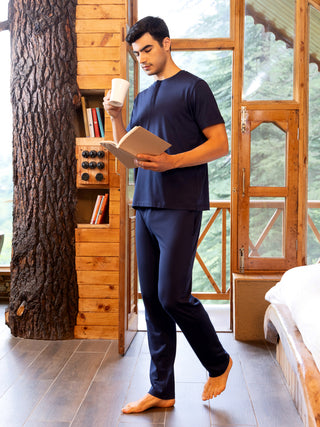 A man in navy blue pajamas is holding a mug and reading a book.
