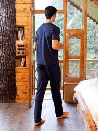 Men in dark blue pajamas standing in a rustic cabin room looking out a window.